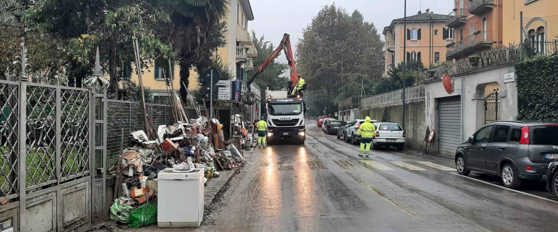 strada con rifiuti dell'alluvione, uomini al lavoro e ruspa